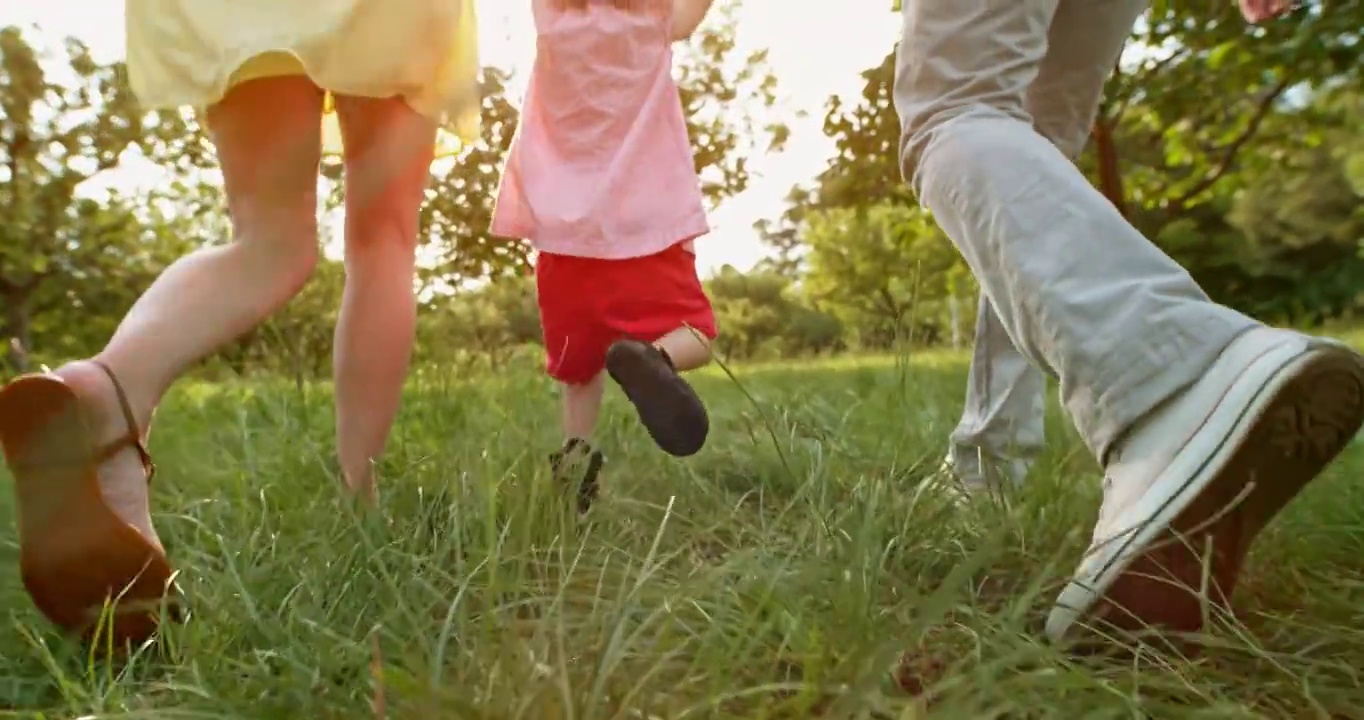一个蹒跚学步的小孩和爸爸妈妈在草地上奔跑时的腿视频素材