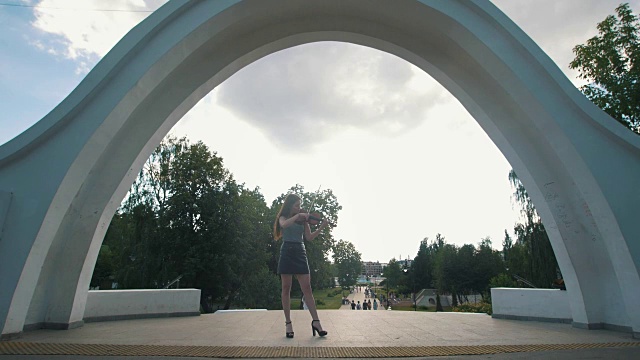 有魅力的女人站在公园前的拱门下拉小提琴视频素材