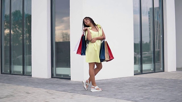 美丽的女孩模特在购物后与彩色的包在手里长连衣裙。缓慢的运动。高清视频素材