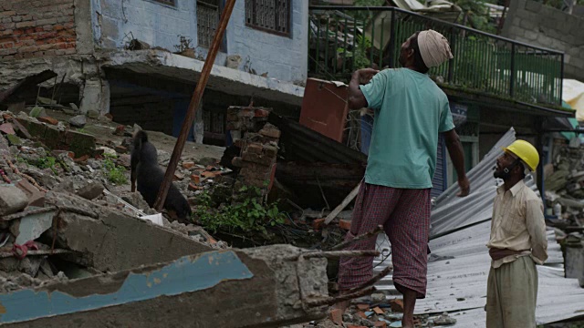 2015年7月31日，尼泊尔Barabise:两名男子和一条狗站在被摧毁的房屋前视频素材