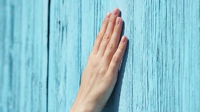 女人的手缓慢地靠在蓝色的木门上。女性手触摸表面的木材视频素材