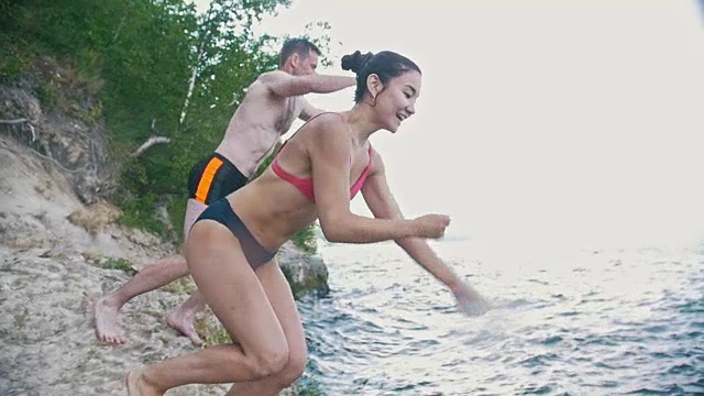 女孩和一个男孩一起在水里跳跃，在大自然中度假，慢镜头视频素材