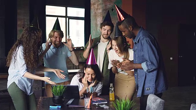 漂亮女人在现代化的办公室工作，同事们带来生日蛋糕和派对帽，女孩吹蜡烛，拍着手享受祝贺。视频下载