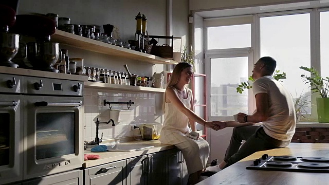 一对幸福的夫妇坐在厨房的台面上聊天，享受着阳光明媚的早晨视频素材