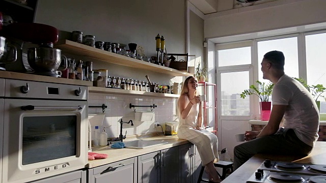 一对快乐的年轻人坐在厨房的台面上聊天，享受着阳光明媚的早晨视频素材