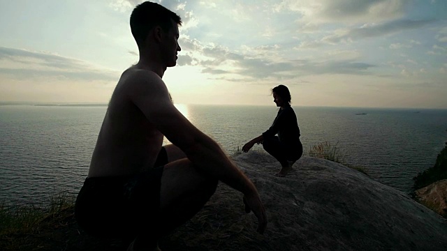 日出时分，年轻男女在巨石上练习瑜伽视频素材