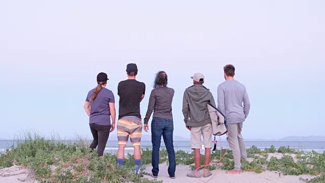 一群年轻的冲浪者站在海滩上看海浪视频素材