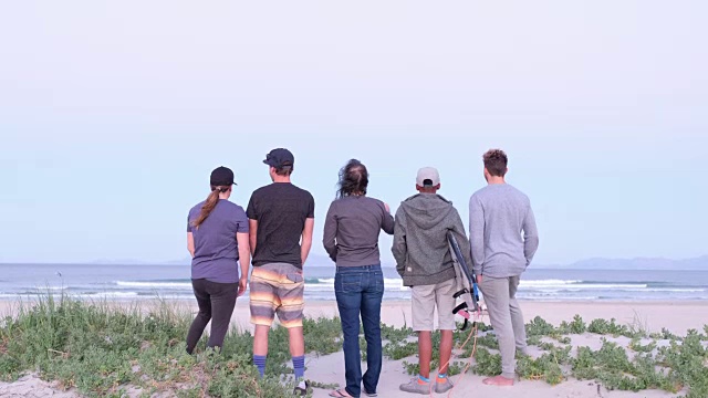一群冲浪者站在海滩上看海浪视频素材