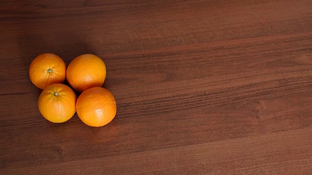 四个成熟多汁的橙子放在棕色的木头表面上。视频下载