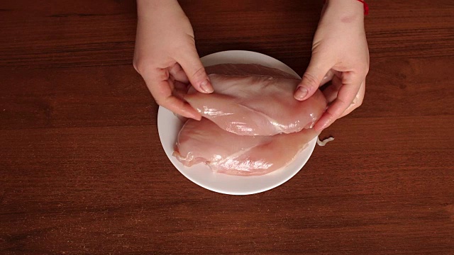 女孩把生鸡肉放在一个白色盘子里。视频下载