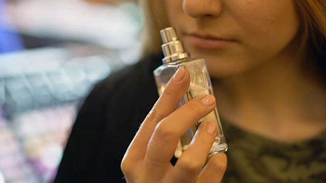 年轻女子在商店闻香水测试员，选择香水，清香视频下载