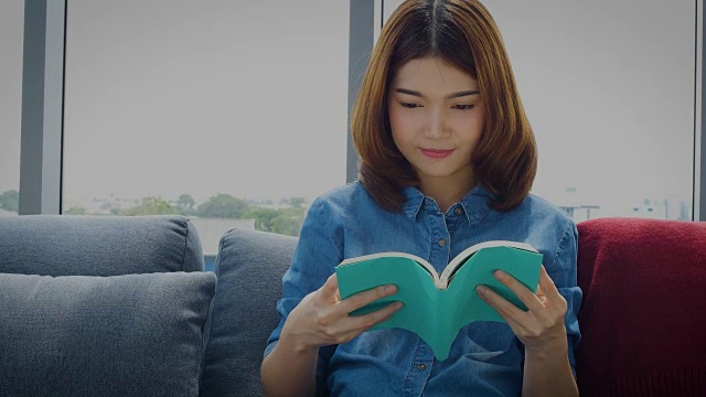 年轻的亚洲女人放松在地板上在家里看书视频下载