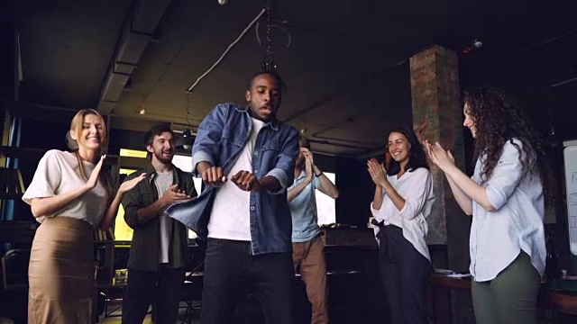 一个快乐的非裔美国人在公司聚会上跳舞的慢动作，而他的团队成员在鼓掌，看着他笑。视频素材