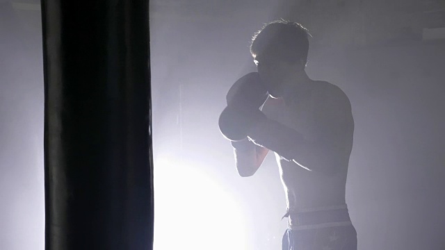 赤膊搏击手在拳击拳击袋在黑暗的房间与烟雾，侧视视频素材