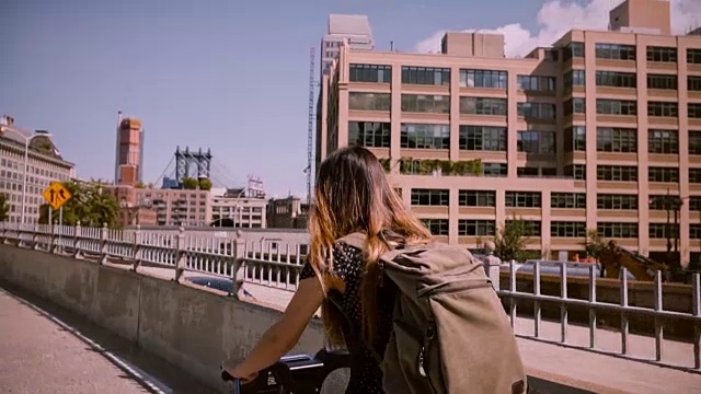 后视图女通勤者骑着自行车与背包和金色的头发在一个阳光明媚的日子的风吹慢动作视频素材