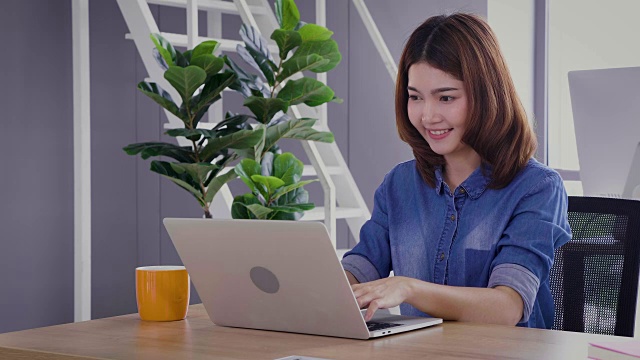 年轻的亚洲商务女性使用笔记本电脑和喝咖啡在办公室工作视频下载