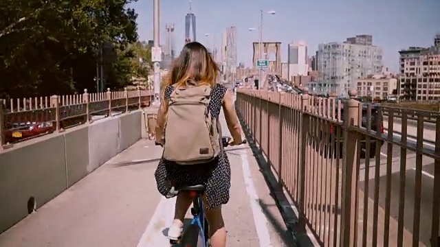 后视图快乐的女人与背包骑自行车沿着一个独立的自行车道水平上的布鲁克林桥，纽约市视频素材