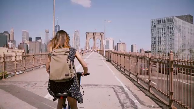 在纽约布鲁克林大桥上，一位黑发女子骑着自行车沿着一条美丽的自行车道骑车视频下载