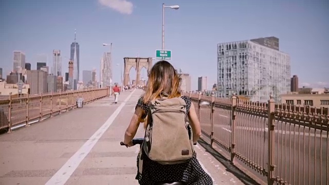 后视图女性自由工作者与长飞扬的头发享受周末骑自行车在布鲁克林大桥，慢镜头视频素材