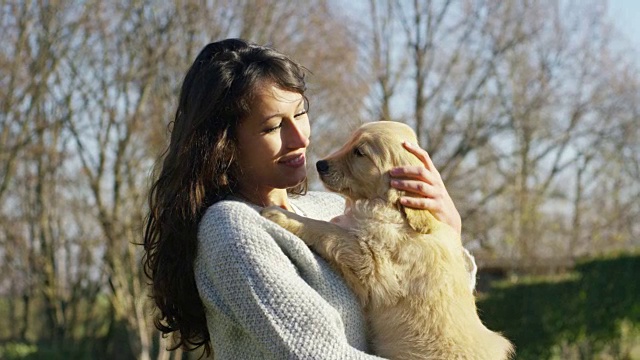 一个女孩拥抱，玩耍，亲吻，训练他的狗品种金毛猎犬的纯种小狗。玩和快乐和微笑。视频素材