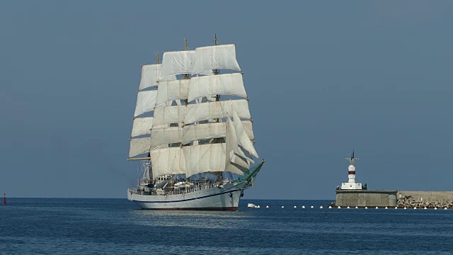 一艘美丽的老式帆船在灯塔的背景下驶入港口视频素材