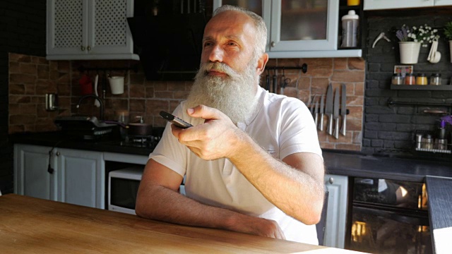 一个留着胡子的老人在厨房里控制电视的遥控器视频下载