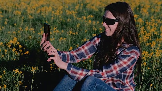 一名女子坐在黄花丛中的草地上自拍。视频下载