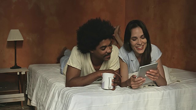 多民族年轻夫妇在床上看数字平板电脑的实时视频视频素材