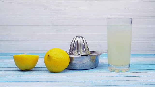 鲜榨生物有机柠檬与不锈钢榨汁机和满杯柠檬水与冰块在蓝色木板滑下运动夏季概念视频下载