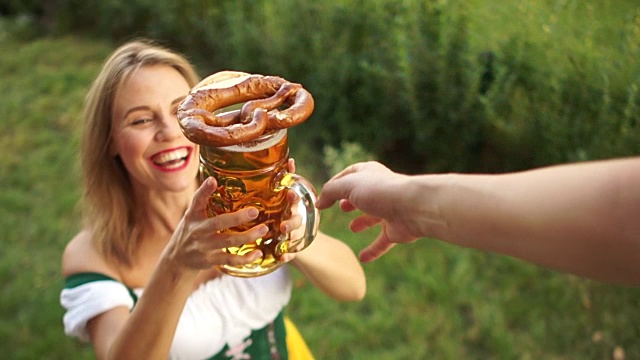 一个穿着传统巴伐利亚连衣裙的女孩在啤酒节上买啤酒和椒盐卷饼。女人笑得很开心，喜欢买东西。在绿色背景上视频素材