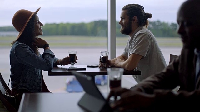 多元化的年轻千禧夫妇在机场候机厅咖啡厅的窗口边聊天。视频素材