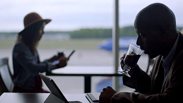 从非洲裔美国商人到年轻的混血女旅行者，在机场候机厅的咖啡馆里喝着咖啡。视频素材