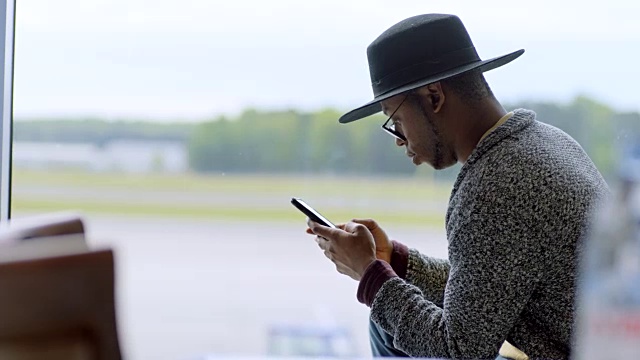 年轻的混血男性旅客在机场登机口窗口用智能手机。视频素材