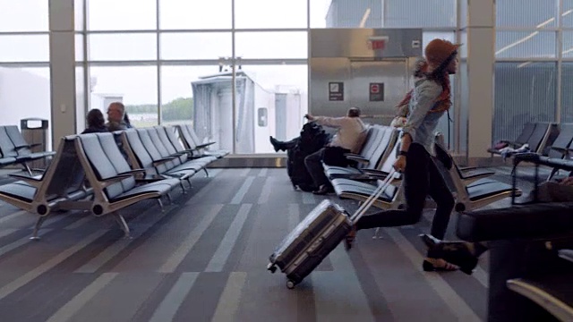 时髦的年轻女子疯狂地跑过机场候机区，跳过行李箱。视频下载