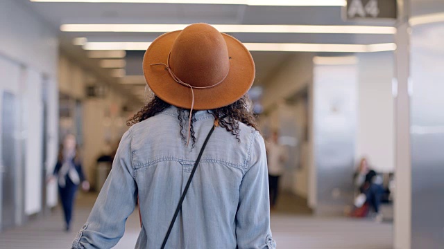 SLO MO:跟着戴着帽子的时髦年轻女子走过机场候机楼。视频素材