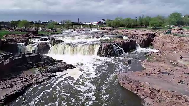 在南达科塔苏福尔斯，一架无人机在流经岩石和瀑布的河水中飞行视频下载