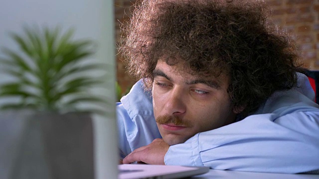 一头卷发的滑稽商人在工作时打瞌睡，在现代办公室的工作场所睡觉视频下载