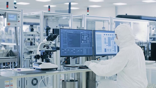 在实验室中，科学家穿着防护服在个人电脑上做研究。现代制造半导体和制药项目。视频素材