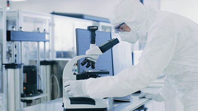在实验室里，科学家穿着防护服用显微镜和个人电脑做研究。现代制造半导体和制药项目。视频素材