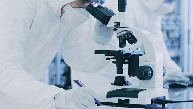 在实验室科学家穿着防护服做研究，使用显微镜和记录数据。工人在一个现代制造生产半导体和药品。视频素材