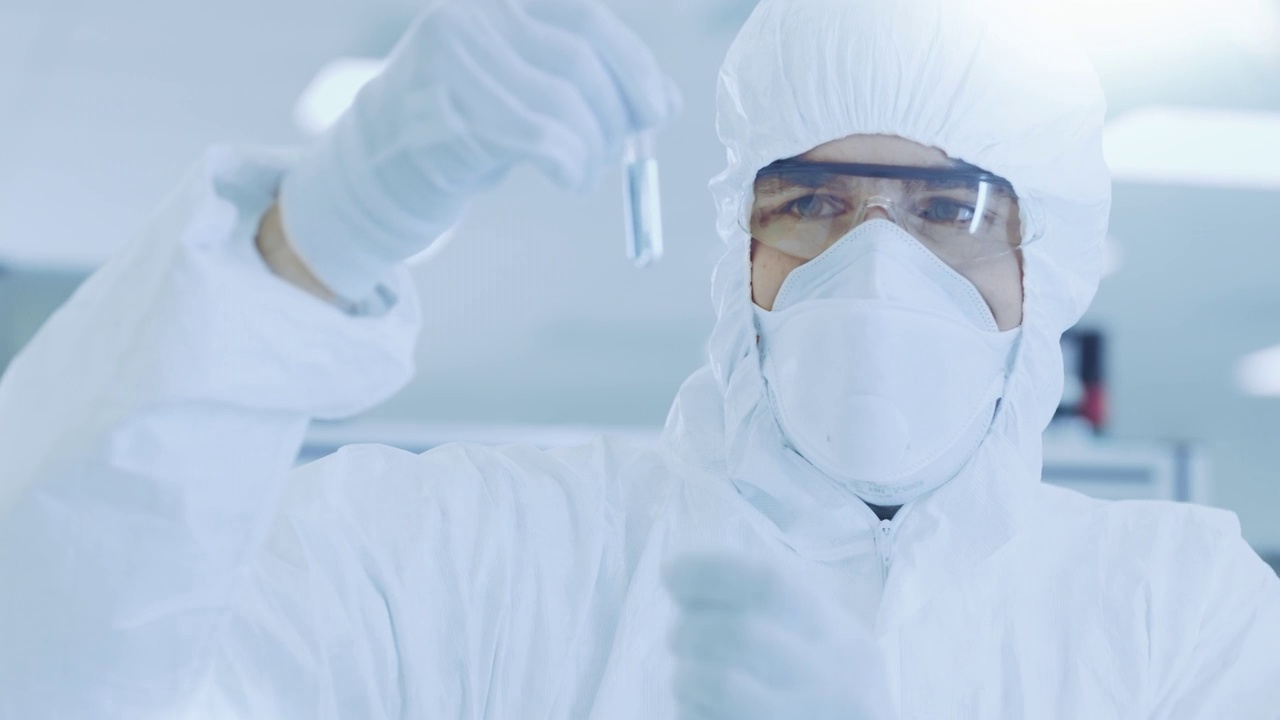在实验室研究员/科学家穿着防护服拿着装有实验药物的试管并看着它。视频素材