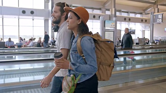 时髦的年轻夫妇手挽着手穿过机场航站楼。跟踪。视频下载