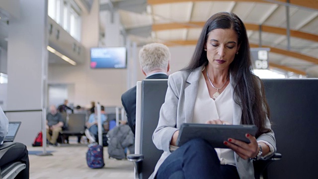 女商人坐在机场候机区靠近登机口的地方用平板电脑工作。视频素材