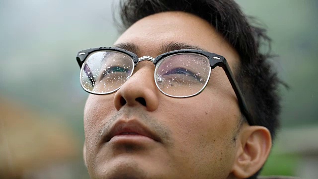 一名亚裔男子戴着眼镜，将脸暴露在雨中视频素材