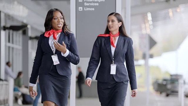 两名不同的女空乘人员在机场外的地面交通工具边走边交谈。视频素材