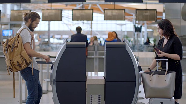 四名不同的旅客使用机场候机楼的自助服务台办理登机手续并取回登机牌。视频素材