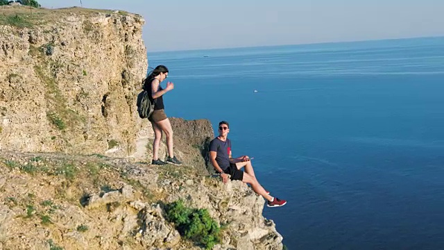 年轻的背包女接近坐在岩石边自拍的男人视频素材