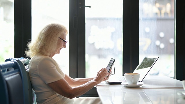 快乐的老年妇女使用手机和笔记本电脑视频素材