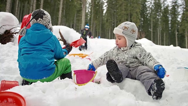 SLO MO蹒跚学步的孩子在雪地里玩，把雪放进塑料桶里视频素材