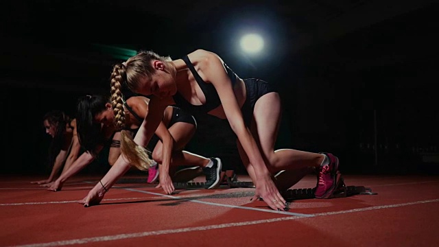 田径场上的女运动员在比赛前蹲在起跑点上。在慢动作视频素材